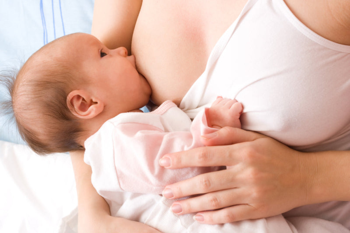 Mère allaitant son nourrisson en position allongée, bébé habillé en rose tenant le sein