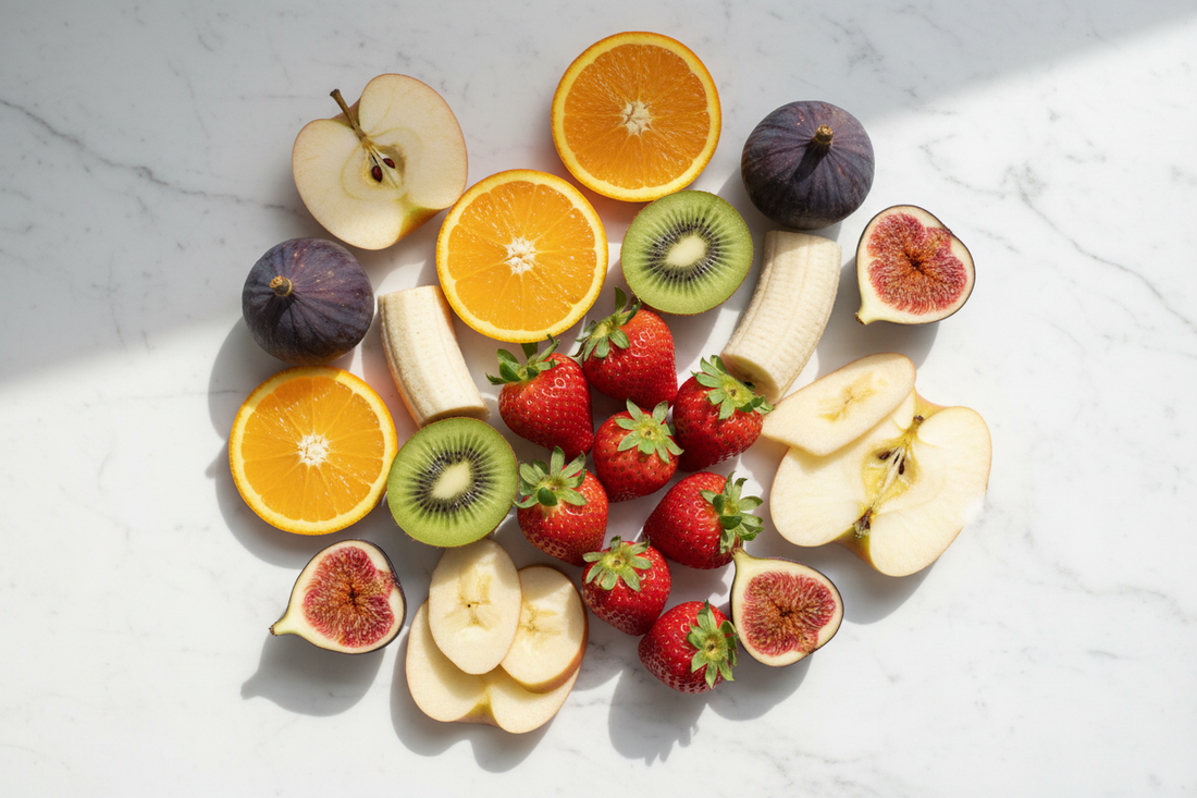 Assortiment de fruits frais de saison — fraises, kiwi, orange, pomme, banane, figues — sur marbre blanc, lumière naturelle matinale